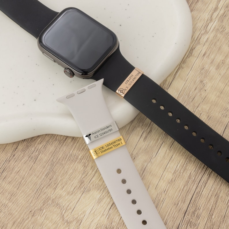 K&ouml;nnte beinhalten: Zwei Smartwatch-Armb&auml;nder mit medizinischen Notfall-ID-Tags. Ein schwarzes Armband hat ein ros&eacute;goldenes Tag mit dem Text "EPILEPSY ICE (123)4567586". Das andere Armband ist hellgrau mit zwei Tags. Ein Tag sagt "Aaron Sanders ICE 123456789". Das andere Tag sagt "ICE: 123456789 Diabetes Type 1".