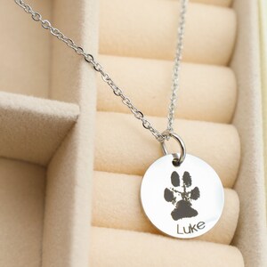 May include: A silver necklace with a round pendant featuring a paw print and the name "Luke" engraved on it.