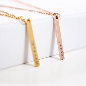 May include: Two gold bar necklaces with personalized engravings. The necklace on the left has the word "love" engraved on it. The necklace on the right has the initials "J & F & K" engraved on it.