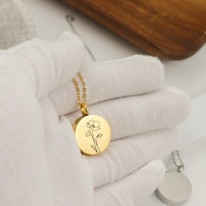 May include: Gold necklace with a round pendant featuring a delicate line drawing of a flower.