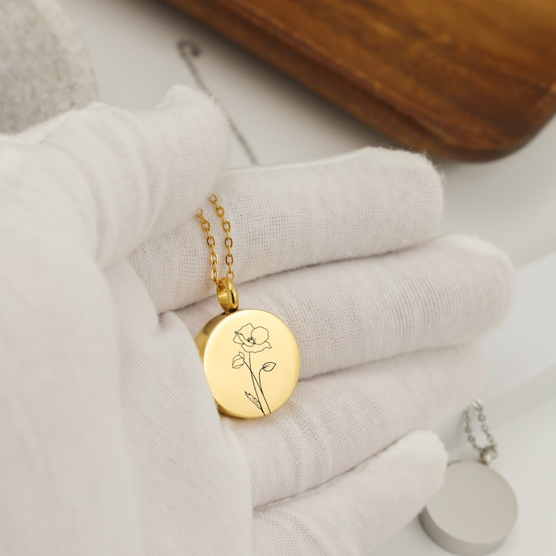 May include: Gold necklace with a round pendant featuring a delicate line drawing of a flower.
