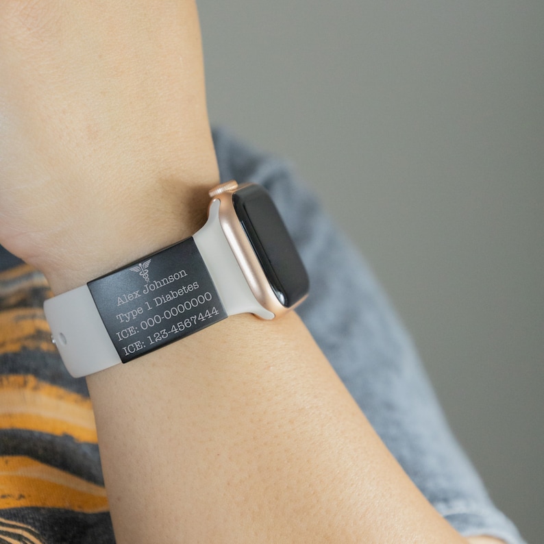 K&ouml;nnte beinhalten: Eine wei&szlig;e Apple Watch mit einem schwarzen medizinischen Alarm-Armband. Das Armband tr&auml;gt den Text "Alex Johnson, Typ-1-Diabetes, ICE: 000-0000000, ICE: 123-4567444" und ein medizinisches Symbol.