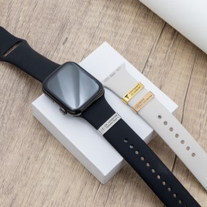 K&ouml;nnte beinhalten: Eine schwarze Smartwatch mit einem schwarzen Armband und einem hellgrauen Armband. Das schwarze Armband hat eine silberne medizinische Notfall-Kennzeichnung. Das hellgraue Armband hat eine goldene medizinische Notfall-Kennzeichnung mit einem medizinischen Symbol.
