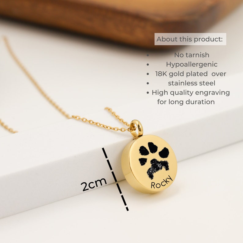 May include: Gold paw print pendant necklace with the name "Rocky" engraved on the front. The pendant is 2 cm in diameter. The necklace is made of hypoallergenic 18K gold plated stainless steel.