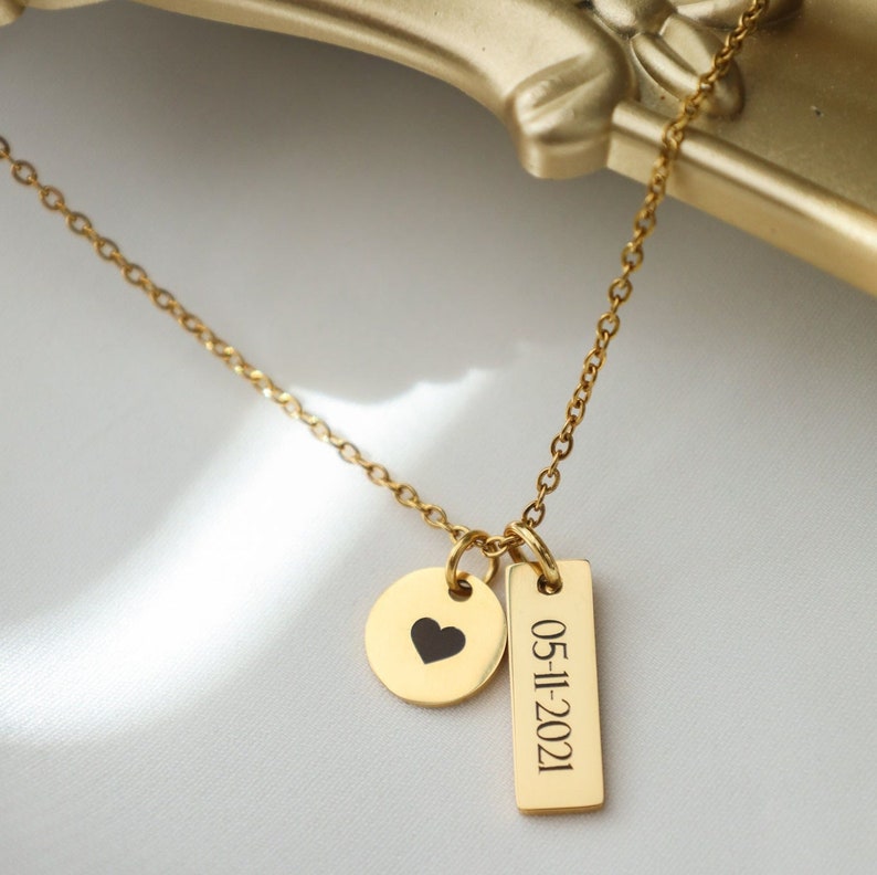 May include: A gold necklace with a small heart charm and a rectangular charm with the date 05-11-2021 engraved on it.