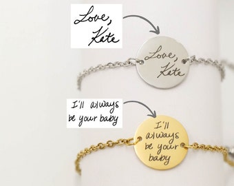 Puede incluir: Dos pulseras con dijes redondos. Una pulsera es plateada con un dije que dice "Love, Kate" en letra manuscrita. La otra pulsera es dorada con un dije que dice "I'll always be your baby" en letra manuscrita.