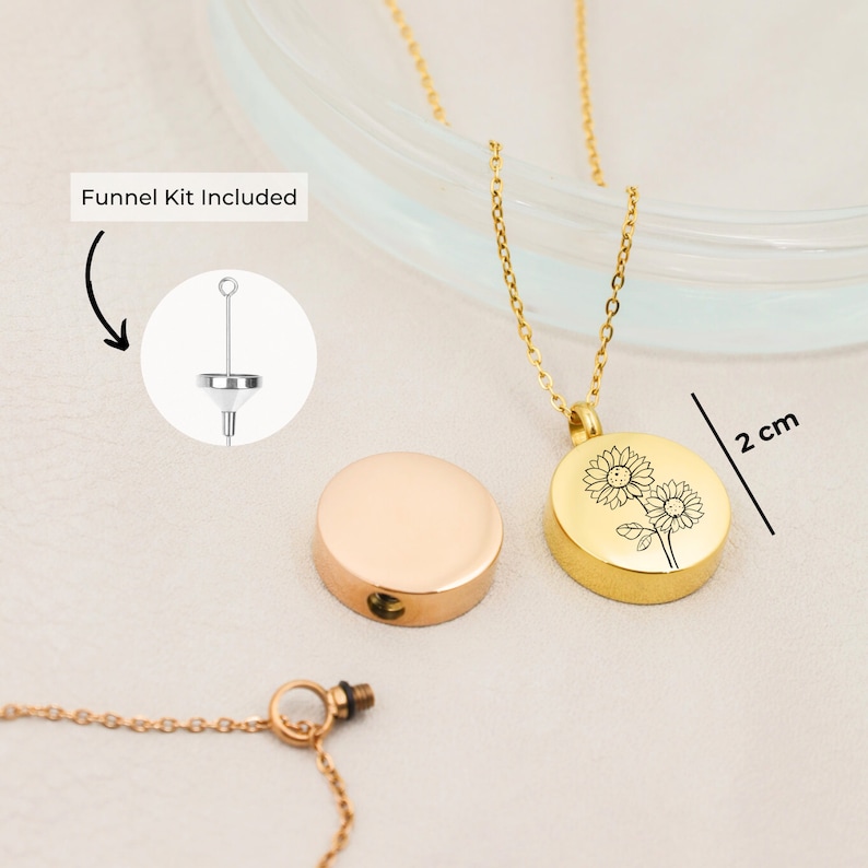 May include: Gold tone necklace with a round pendant featuring an engraved sunflower design. The pendant is 2 cm in diameter and opens to reveal a compartment for holding ashes or other mementos. A funnel kit is included for filling the pendant.