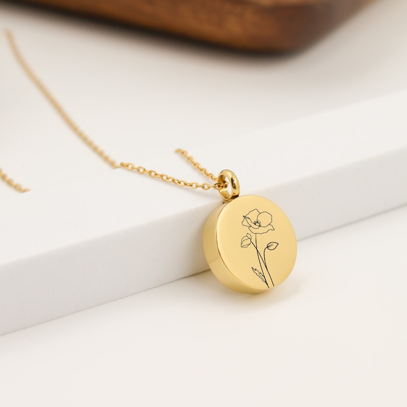 May include: Gold necklace with a round pendant featuring a delicate line drawing of a poppy flower.