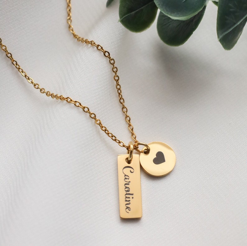 May include: A gold necklace with a heart charm and a rectangular tag engraved with the name "Caroline".