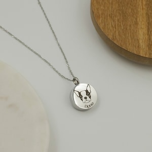 May include: Silver chain necklace with a round pendant featuring an engraved image of a Boston Terrier dog and the name "Ephie".