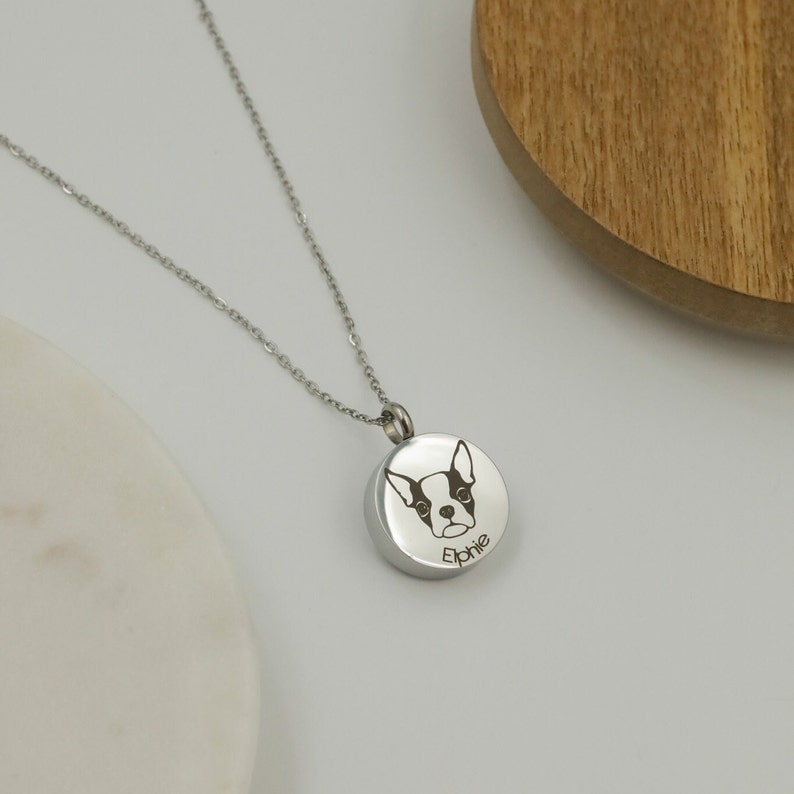 May include: Silver chain necklace with a round pendant featuring an engraved image of a Boston Terrier dog and the name "Ephie".