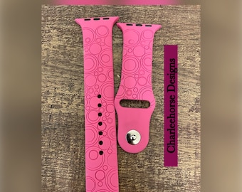 May include: A pink Apple Watch band with a circle pattern. The band is made of silicone and has a black trim. The text "Charleehorse Designs" is visible on the right side of the image.