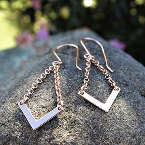 May include: Rose gold earrings with a geometric V-shaped design and a delicate chain.
