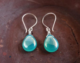 May include: A pair of drop earrings featuring smooth, teardrop-shaped teal stones suspended from silver-toned wire hooks. Each stone is secured with a small silver-toned wire wrap at the top, creating a simple, dangling design with a polished finish.