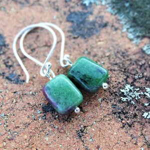 May include: A pair of silver dangle earrings with green and purple square-shaped gemstones.