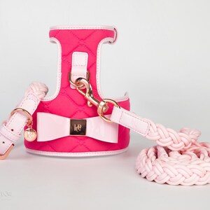 Pink quilted dog harness with a matching pink braided lead and a pink bow with gold accents. The harness has a gold clasp and the lead has a gold buckle.