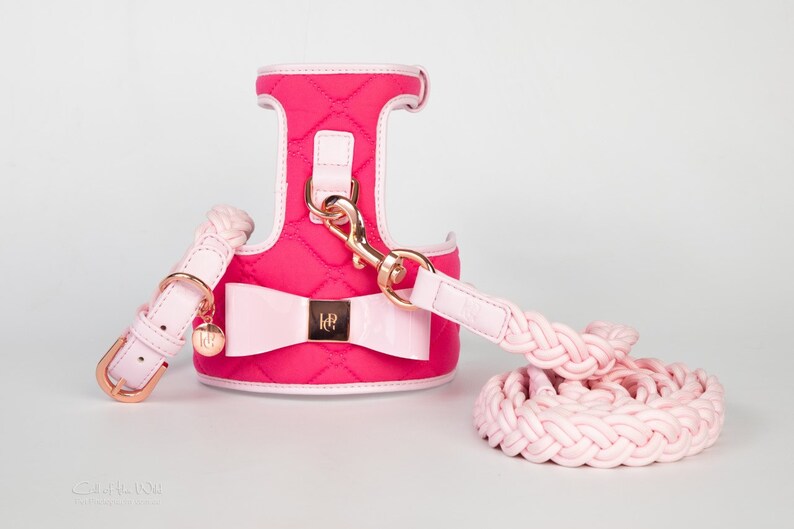 Pink quilted dog harness with a matching pink braided lead and a pink bow with gold accents. The harness has a gold clasp and the lead has a gold buckle.