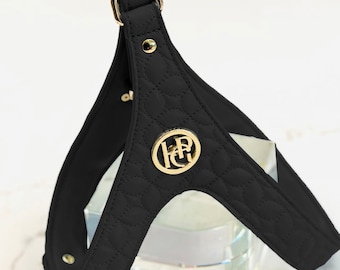 May include: Black quilted dog harness with gold-colored hardware. The harness features a gold emblem with the letters "FR" and a decorative quilted pattern. The harness has a ring at the top for leash attachment.