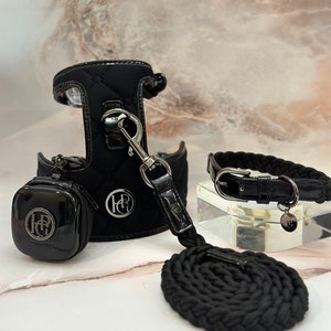 Black quilted dog harness with a matching leash and collar. The harness has a small pouch attached to it. The collar and leash have a silver buckle and a silver charm with the letters "HR" on it.