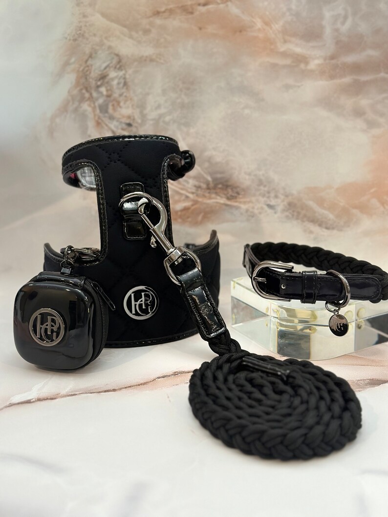 Black quilted dog harness with a matching leash and collar. The harness has a small pouch attached to it. The collar and leash have a silver buckle and a silver charm with the letters "HR" on it.