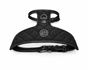 May include: Black quilted dog harness with a metal logo and buckle closure. The harness features a diamond pattern and adjustable straps for a comfortable fit. The harness has a D-ring for leash attachment.