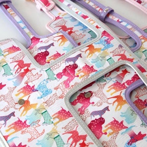 A close-up of a white fabric with a repeating pattern of colourful dogs. The fabric is trimmed with a silver and lavender coloured trim.