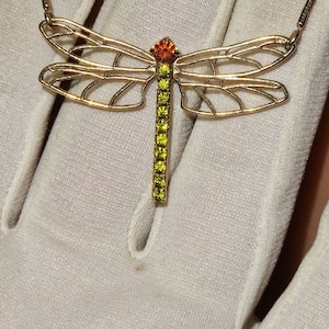 May include: A gold dragonfly necklace with green and orange crystal accents.
