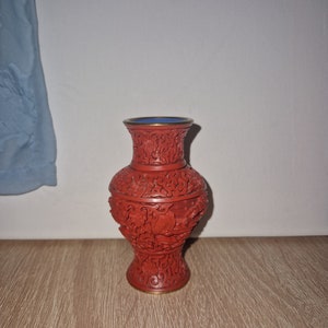 May include: A red, intricately carved vase with a gold rim and a blue interior. The vase is decorated with floral and geometric patterns.