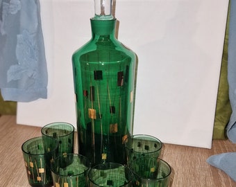 Puede incluir: Un juego de siete decantadores de vidrio verde con diseños geométricos dorados. Los decantadores están dispuestos en círculo sobre una superficie de madera.