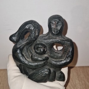 May include: A black carved wooden sculpture of a family. The sculpture depicts a mother holding a child in her arms, with a woman standing behind them. The sculpture is abstract and stylized.