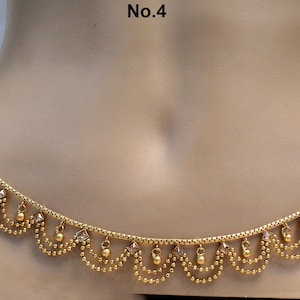 May include: A gold-colored belly chain with a decorative scalloped design. The chain features small, dangling beads and square-shaped accents. The text "No.4" is visible in the upper left corner. This piece is a type of body jewelry.