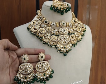 May include: A gold-toned jewelry set with green accents, including a necklace, earrings, and a headpiece. The necklace and earrings feature intricate floral designs with white and green stones. The set is displayed on a mannequin.
