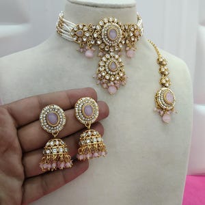 May include: A pink and gold jewelry set, including a choker necklace, earrings, and a headpiece, displayed on a mannequin. The choker features white beads and gold filigree with pink accents. The earrings and headpiece mirror the design. The text "No.5 - Pink" is visible.
