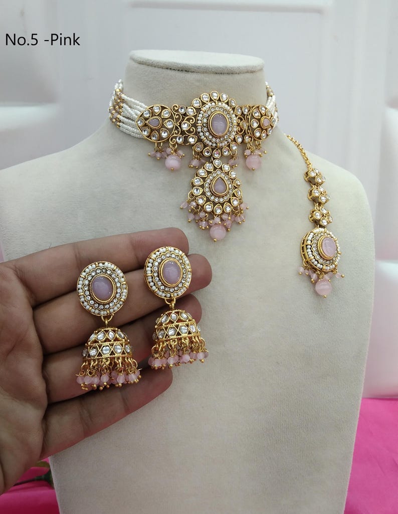 May include: A pink and gold jewelry set, including a choker necklace, earrings, and a headpiece, displayed on a mannequin. The choker features white beads and gold filigree with pink accents. The earrings and headpiece mirror the design. The text "No.5 - Pink" is visible.