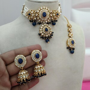 May include: A blue and gold jewelry set, including a choker necklace, earrings, and a headpiece. The set features blue gemstones and white accents. The earrings are held by a hand. The text "No.3- Blue" is in the top left corner.
