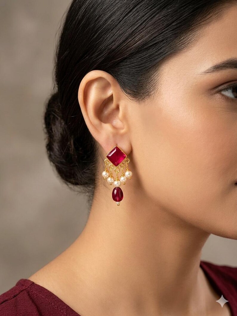 May include: A gold-toned earring featuring a square-cut deep pink gemstone at the top, suspended with a series of small white pearls and a single teardrop-shaped deep pink gemstone at the base, creating a dangling, multi-layered design.