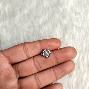 May include: A silver nose ring with a circular design featuring a small flower in the center.