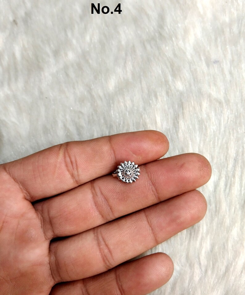 May include: A silver nose ring with a circular design featuring a small flower in the center.