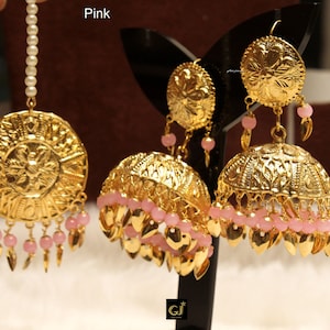 Könnte beinhalten: Goldene Ohrringe mit rosa Perlen und einem Blumenmuster. Die Ohrringe haben die Form einer Kuppel mit einer runden Oberseite. Die Ohrringe hängen an einem goldenen Haken.