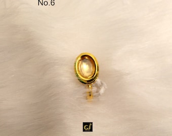 May include: A gold-colored oval-shaped ring with a clear stone in the center. The ring is on a white fuzzy surface. No. 6 is written in the top left corner of the image.
