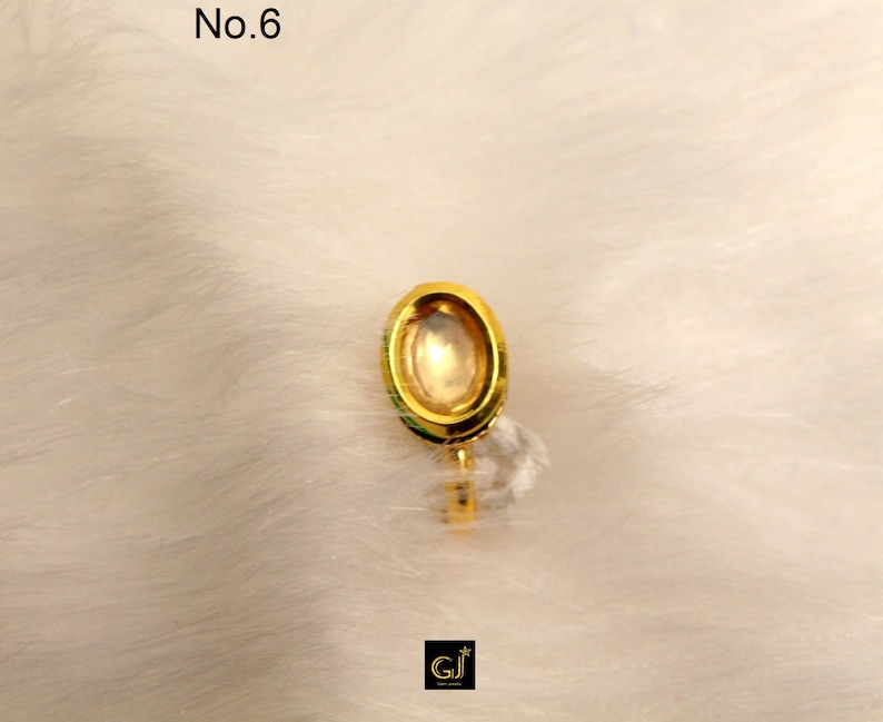 May include: A gold-colored oval-shaped ring with a clear stone in the center. The ring is on a white fuzzy surface. No. 6 is written in the top left corner of the image.