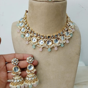 Puede incluir: Un collar de oro con un diseño de múltiples capas que presenta piedras transparentes redondas y cuadradas, acentuado con perlas blancas y cuentas de color azul claro y rosa. Pendientes a juego con un diseño similar y cuentas colgantes de color azul claro y rosa.