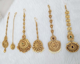 May include: Five gold-toned headpieces with intricate designs and embellishments. Each piece features a circular pendant with a floral motif and a dangling chain. Some pendants have pearl accents.