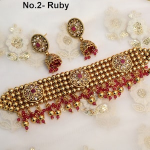May include: Gold choker necklace with red beads and three round pendants featuring white stones and a pink centre stone. Matching earrings with a pink stone and white stones.