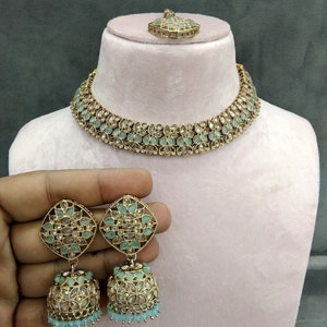 Op de afbeelding: Een gouden ketting met een ontwerp van zeegroene stenen, bijpassende oorbellen met een vierkante bovenkant en een hangende bel, en een hanger. Nr. 1 - Zeegroen.