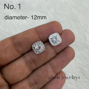 May include: A pair of square-shaped stud earrings with a central clear stone surrounded by smaller stones. The earrings are set in a silver-colored metal. The text "No. 1 diameter- 12mm" is visible. The text "glam jewelrys" is also visible.