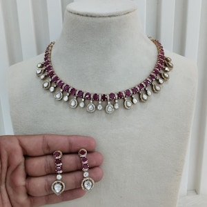 May include: A ruby necklace and matching earrings set displayed on a mannequin. The necklace features a series of ruby-coloured stones and clear, teardrop-shaped accents. The earrings are held in a hand and have a similar design. The text "No.1- Ruby" and "Glam jewelrys" are visible.