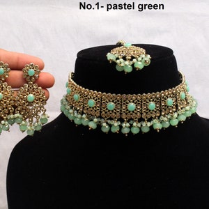 May include: A gold choker necklace with pastel green stones and beads. Matching earrings with pastel green stones and beads. The necklace and earrings are on a black background. No. 1 - pastel green.