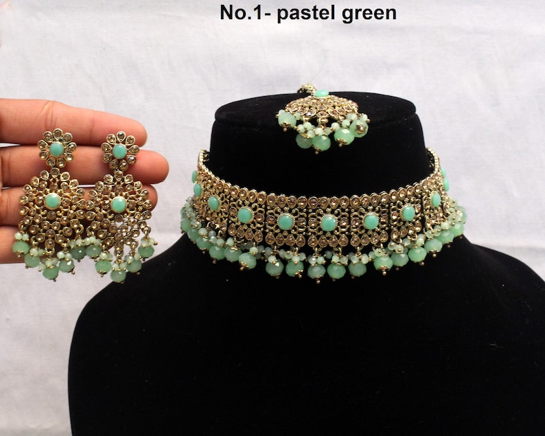 May include: A gold choker necklace with pastel green stones and beads. Matching earrings with pastel green stones and beads. The necklace and earrings are on a black background. No. 1 - pastel green.