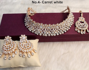 May include: A gold-tone necklace and earrings set with clear rhinestones. The necklace is a choker style with multiple layers of rhinestones. The earrings are dangle style with a round shape and multiple layers of rhinestones. The set is displayed on a burgundy box and a cream-colored pillow.
